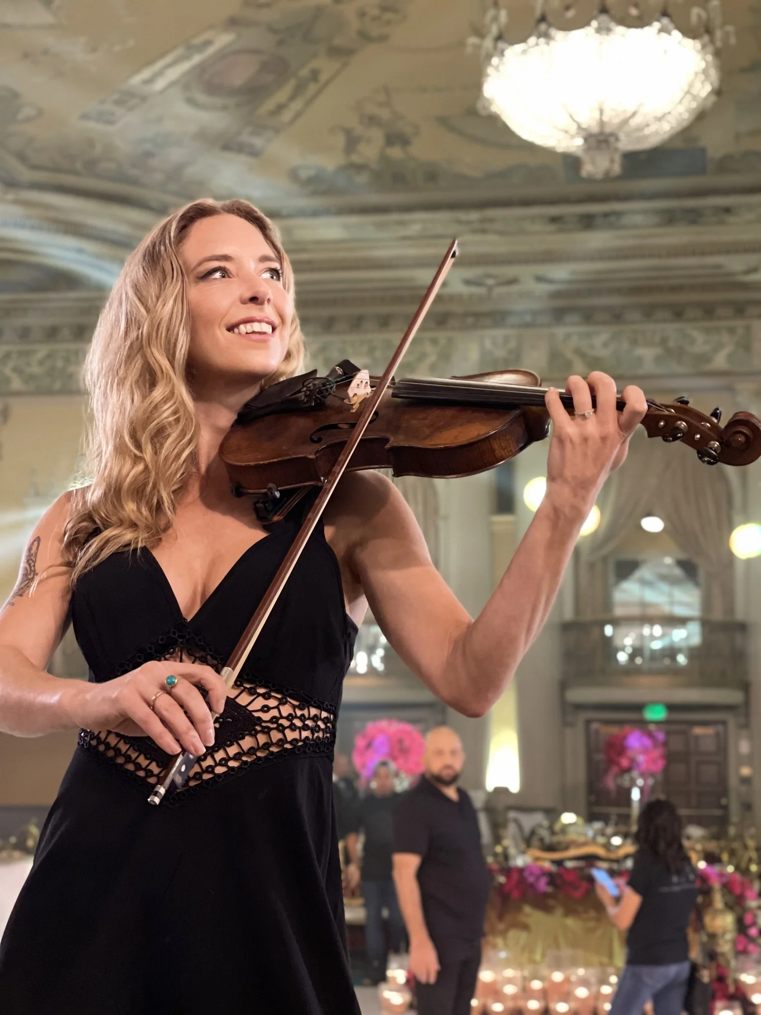 Elin Wolf performing violin in a black gown inside an ornate ballroom